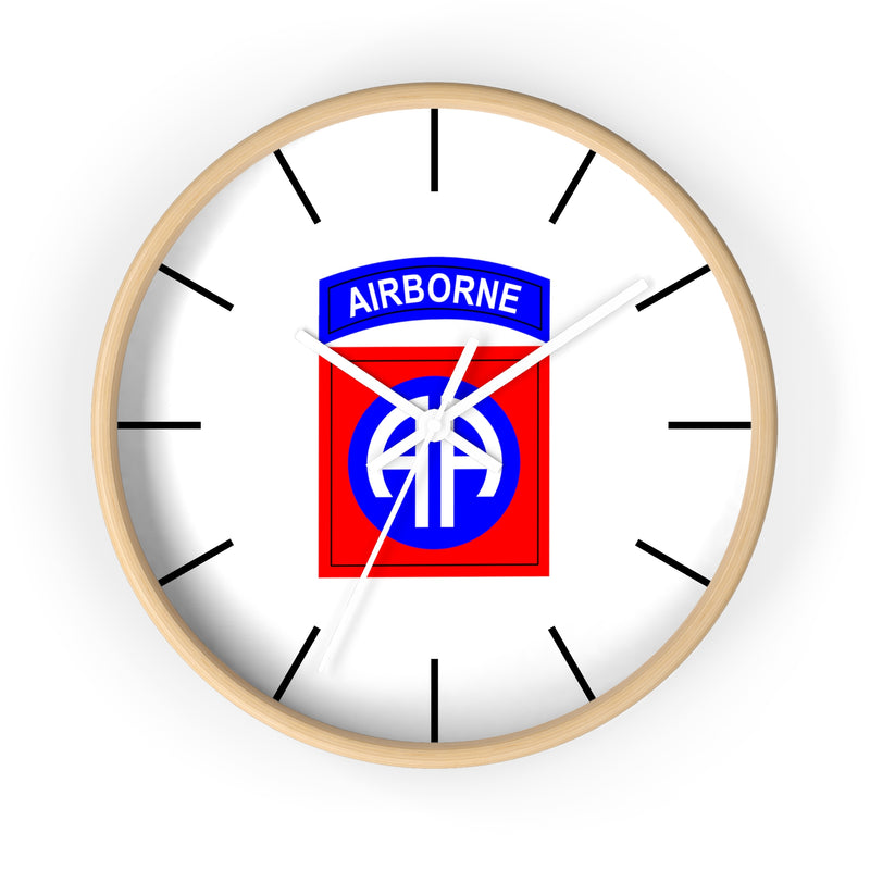 The 82nd Airborne Wall Clock boasts a light wooden frame and a silent clock mechanism. At its center, it prominently displays the 82nd Airborne Division insignia: "AIRBORNE" in blue on a white arch above a blue "AA" on a red background. Black tick marks are used for the hours, making it an excellent addition to any personalized environment.
