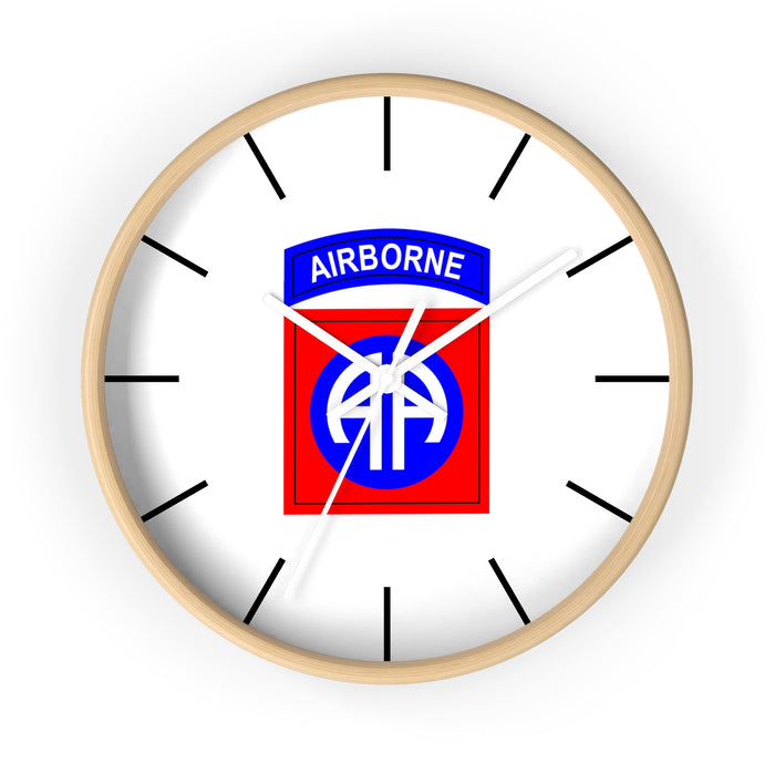 The 82nd Airborne Wall Clock boasts a light wooden frame and a silent clock mechanism. At its center, it prominently displays the 82nd Airborne Division insignia: "AIRBORNE" in blue on a white arch above a blue "AA" on a red background. Black tick marks are used for the hours, making it an excellent addition to any personalized environment.