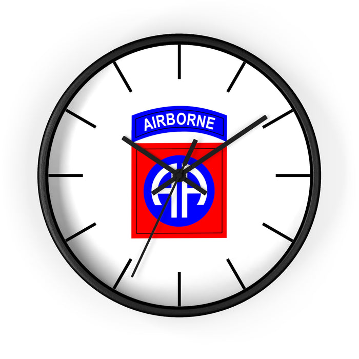 The 82nd Airborne Wall Clock is a round timepiece with a black frame and white face, featuring a stylized "AIRBORNE" insignia in the center. It showcases a white parachute over a blue background with the word "AIRBORNE" in white on a blue tab above it. Additionally, it boasts silent clock mechanisms, perfect for creating your personalized environment.