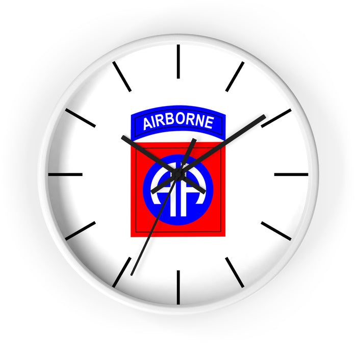 The 82nd Airborne Wall Clock is a high-quality round timepiece featuring a white face and black hour markers, displaying the time at approximately 10:10. At its center is the distinctive insignia of the U.S. Army 82nd Airborne Division, which includes a blue arch with "AIRBORNE" text above a red square displaying "AA" in white letters—an excellent addition to any personalized environment.