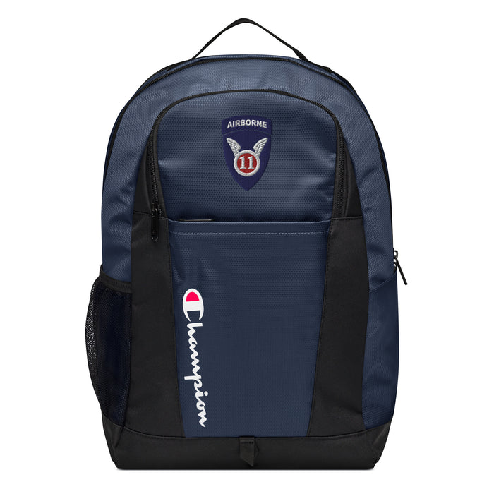 The 11th Airborne Division Champion Backpack in dark blue and black showcases a "Champion" logo, a mesh side pocket, a top handle and a 11th Airborne Division logo on the front. Crafted from water-resistant material, this sports backpack is ideal for all-weather use.