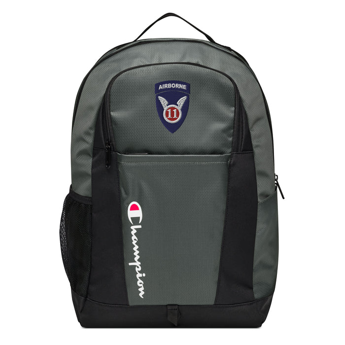 The 11th Airborne Division Champion Backpack in gray and black showcases a "Champion" logo, a mesh side pocket, a top handle and a 11th Airborne Division logo on the front. Crafted from water-resistant material, this sports backpack is ideal for all-weather use.