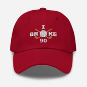 The "I Broke 90" Men's Embroidered Hat is a cranberry, low-profile hat featuring the phrase "I Broke 70" on the front. The word "Broke" is uniquely stylized with a golf ball as the 'O' and crossed golf clubs beneath it.