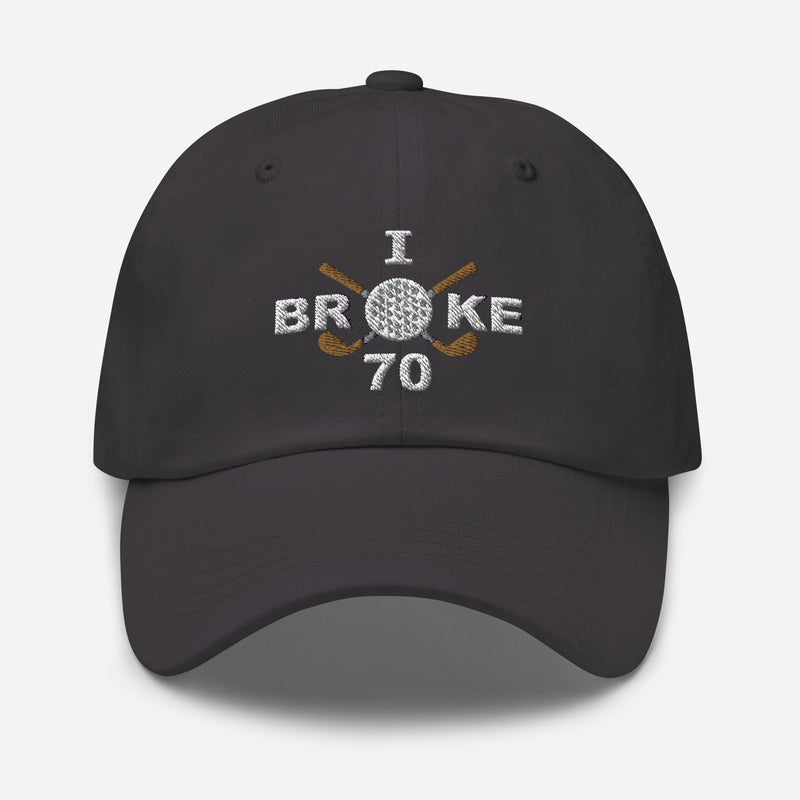 The "I Broke 70" Men's Embroidered Hat is a dark grey, low-profile hat featuring the phrase "I Broke 70" on the front. The word "Broke" is uniquely stylized with a golf ball as the 'O' and crossed golf clubs beneath it.