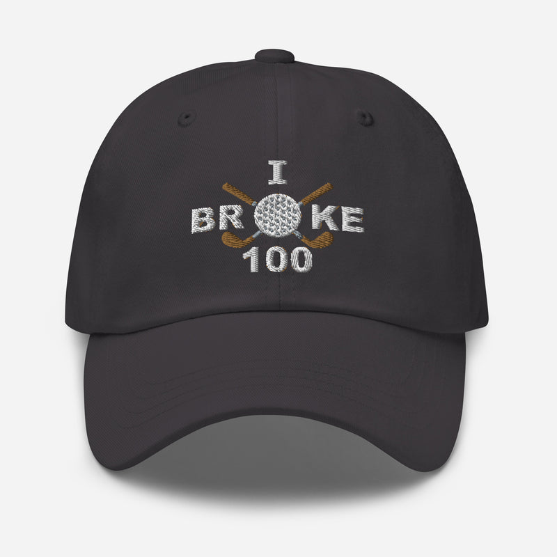 The "I Broke 100" Men's Embroidered Hat is a dark grey, low-profile hat featuring the phrase "I Broke 70" on the front. The word "Broke" is uniquely stylized with a golf ball as the 'O' and crossed golf clubs beneath it.