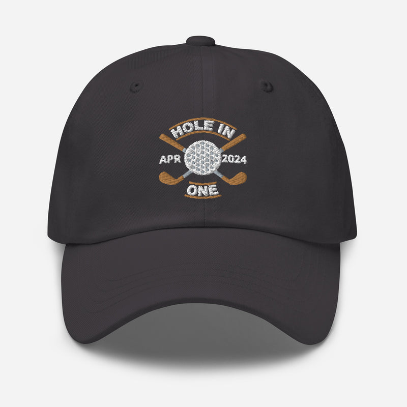 The Golf Hat in dark grey - Hole in One with Personalized Month and Year features a golf design  including two crossed golf clubs with a golf ball at the center and the text "HOLE IN ONE" above. Customized month and year are on the left and right sides.