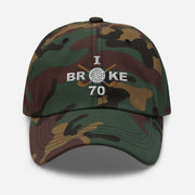 The "I Broke 70" Men's Embroidered Hat is a green camouflage, low-profile hat featuring the phrase "I Broke 70" on the front. The word "Broke" is uniquely stylized with a golf ball as the 'O' and crossed golf clubs beneath it.