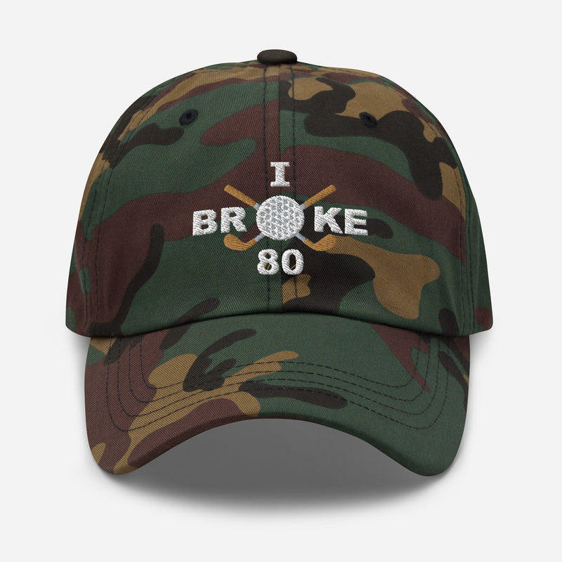 The "I Broke 80" Men's Embroidered Hat is a green camouflage, low-profile hat featuring the phrase "I Broke 70" on the front. The word "Broke" is uniquely stylized with a golf ball as the 'O' and crossed golf clubs beneath it.