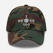 The "I Broke 100" Men's Embroidered Hat is a green camouflage, low-profile hat featuring the phrase "I Broke 70" on the front. The word "Broke" is uniquely stylized with a golf ball as the 'O' and crossed golf clubs beneath it.