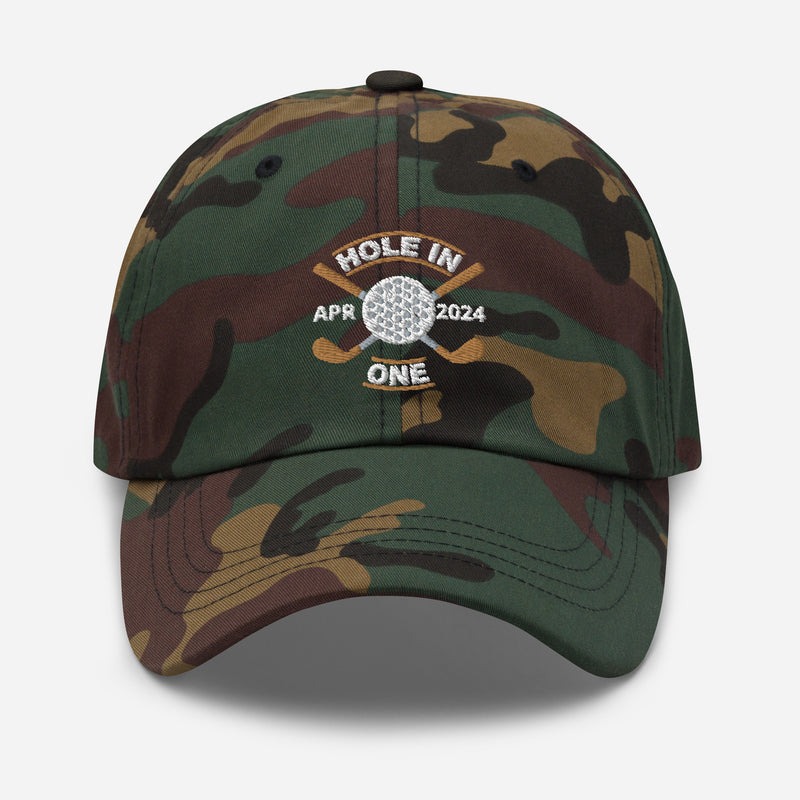 The Golf Hat in green camouflage - Hole in One with Personalized Month and Year features a golf design  including two crossed golf clubs with a golf ball at the center and the text "HOLE IN ONE" above. Customized month and year are on the left and right sides.