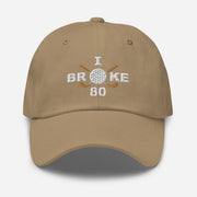 The "I Broke 80" Men's Embroidered Hat is a khaki colored, low-profile hat featuring the phrase "I Broke 70" on the front. The word "Broke" is uniquely stylized with a golf ball as the 'O' and crossed golf clubs beneath it.