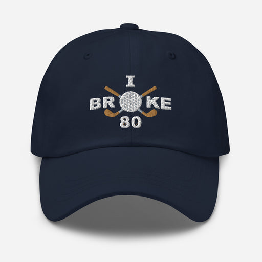 The "I Broke 80" Men's Embroidered Hat is a navy, low-profile hat featuring the phrase "I Broke 70" on the front. The word "Broke" is uniquely stylized with a golf ball as the 'O' and crossed golf clubs beneath it.