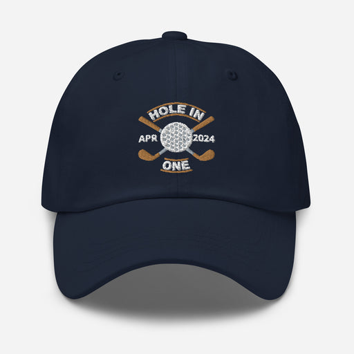 The Golf Hat in navy - Hole in One with Personalized Month and Year features a golf design  including two crossed golf clubs with a golf ball at the center and the text "HOLE IN ONE" above. Customized month and year are on the left and right sides.