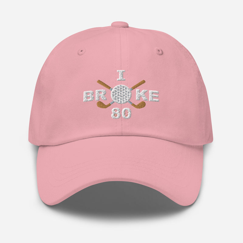 The "I Broke 80" Men's Embroidered Hat is a pink, low-profile hat featuring the phrase "I Broke 70" on the front. The word "Broke" is uniquely stylized with a golf ball as the 'O' and crossed golf clubs beneath it.