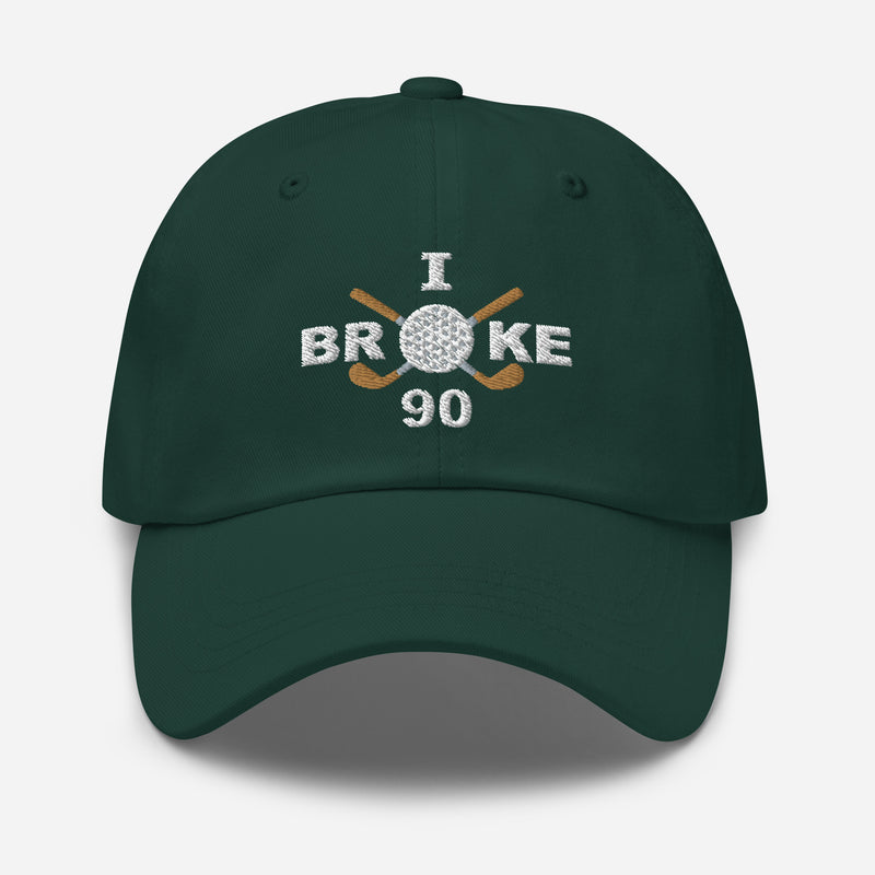 The "I Broke 90" Men's Embroidered Hat is a spruce colored, low-profile hat featuring the phrase "I Broke 70" on the front. The word "Broke" is uniquely stylized with a golf ball as the 'O' and crossed golf clubs beneath it.