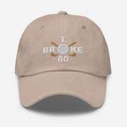 The "I Broke 80" Men's Embroidered Hat is a stone colored, low-profile hat featuring the phrase "I Broke 70" on the front. The word "Broke" is uniquely stylized with a golf ball as the 'O' and crossed golf clubs beneath it.