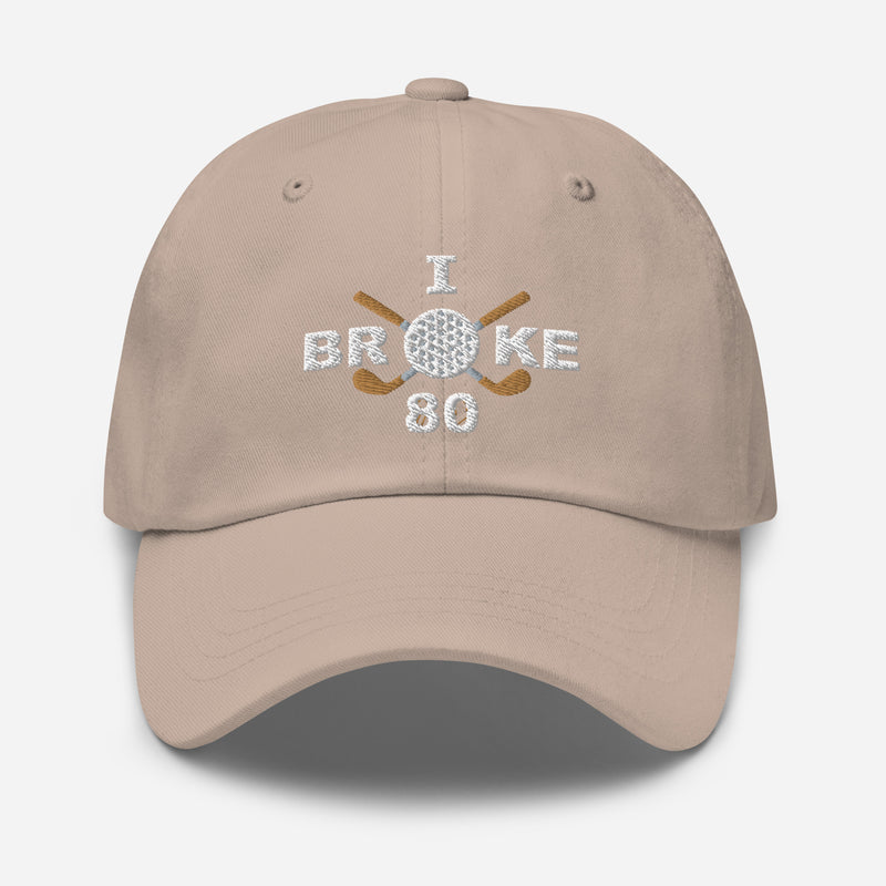 The "I Broke 80" Men's Embroidered Hat is a stone colored, low-profile hat featuring the phrase "I Broke 70" on the front. The word "Broke" is uniquely stylized with a golf ball as the 'O' and crossed golf clubs beneath it.