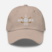 The "I Broke 90" Men's Embroidered Hat is a stone colored, low-profile hat featuring the phrase "I Broke 70" on the front. The word "Broke" is uniquely stylized with a golf ball as the 'O' and crossed golf clubs beneath it.