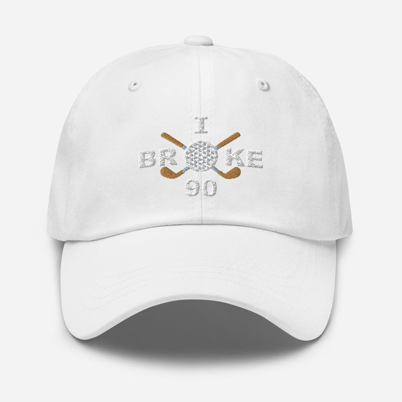 The "I Broke 90" Men's Embroidered Hat is a white, low-profile hat featuring the phrase "I Broke 70" on the front. The word "Broke" is uniquely stylized with a golf ball as the 'O' and crossed golf clubs beneath it.