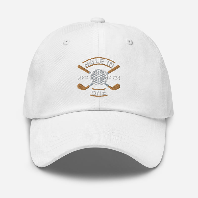 The Golf Hat in white - Hole in One with Personalized Month and Year features a golf design  including two crossed golf clubs with a golf ball at the center and the text "HOLE IN ONE" above. Customized month and year are on the left and right sides.