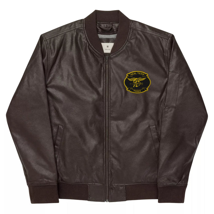 A timeless addition, this Navy Seal Team 3 Embroidered Leather Bomber Jacket is made from black PU leather. It includes a zippered front, ribbed cuffs and collar, and an embroidered emblem of a golden eagle with trident and anchor on the left chest, with "NAVY SEAL TEAM" above and "THREE" below.