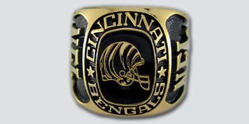 A gold colored paperweight featuring the Cincinnati Bengals logo set against a black enamel background. The words "Cincinnati Bengals" are engraved on the bezel.
