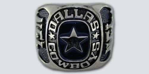 A silver colored paperweight featuring the Dallas Cowboys logo set against a dark blue enamel background. The words "Dallas Cowboys" are engraved on the bezel.