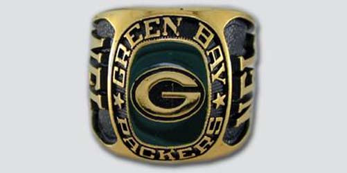 A gold colored paperweight featuring the Green Bay Packers logo set against a green enamel background. The words "Green Bay Packers" are engraved on the bezel.