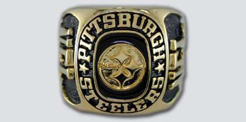 A gold colored paperweight featuring the Pittsburgh Steelers logo set against a black enamel background. The words "Pittsburgh Steelers" are engraved on the bezel.