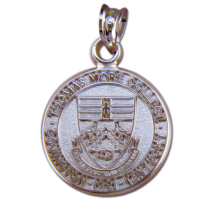 The Thomas More College Seal Silver Pendant is meticulously crafted from sterling silver and showcases the engraved emblem of Thomas More College. Inscribed along the edge are the words "Thomas More College, Covington, 1921, Kentucky." At its center lies a detailed depiction of the college crest, adorned with intricate symbols and patterns.