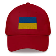 A cranberry colored Ukrainian Flag Hat with the logo on the front.  The hat has a curved visor and an adjustable strap at the back.