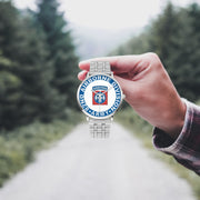 A hand in a plaid shirt holds the 82nd Airborne Division Silvertone Watch against the background of a blurred forest scene, where a path runs through the center.