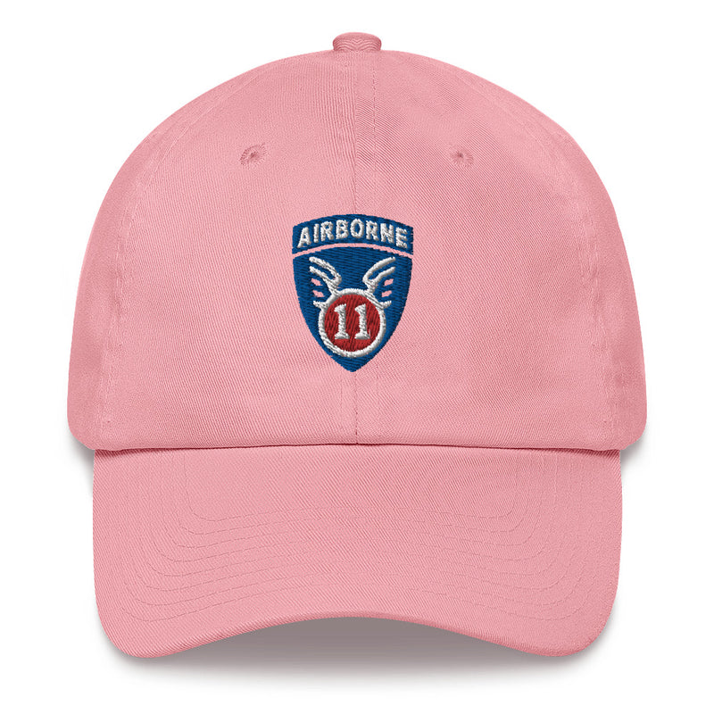 A pink 11th Airborne Division Hat with the logo on the front.  The hat has a curved visor and an adjustable strap at the back.