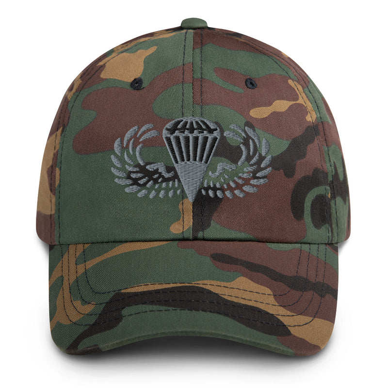 A military style Basic Parachutist Hat with camouflage and the logo on the front.  The hat has a curved visor and an adjustable strap at the back. 