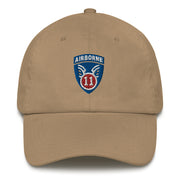 A khaki colored 11th Airborne Division Hat with the logo on the front.  The hat has a curved visor and an adjustable strap at the back.