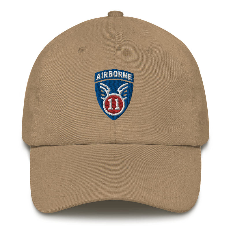 A khaki colored 11th Airborne Division Hat with the logo on the front.  The hat has a curved visor and an adjustable strap at the back.