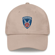 A stone colored 11th Airborne Division Hat with the logo on the front.  The hat has a curved visor and an adjustable strap at the back.