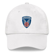 A white 11th Airborne Division Hat with the logo on the front.  The hat has a curved visor and an adjustable strap at the back.